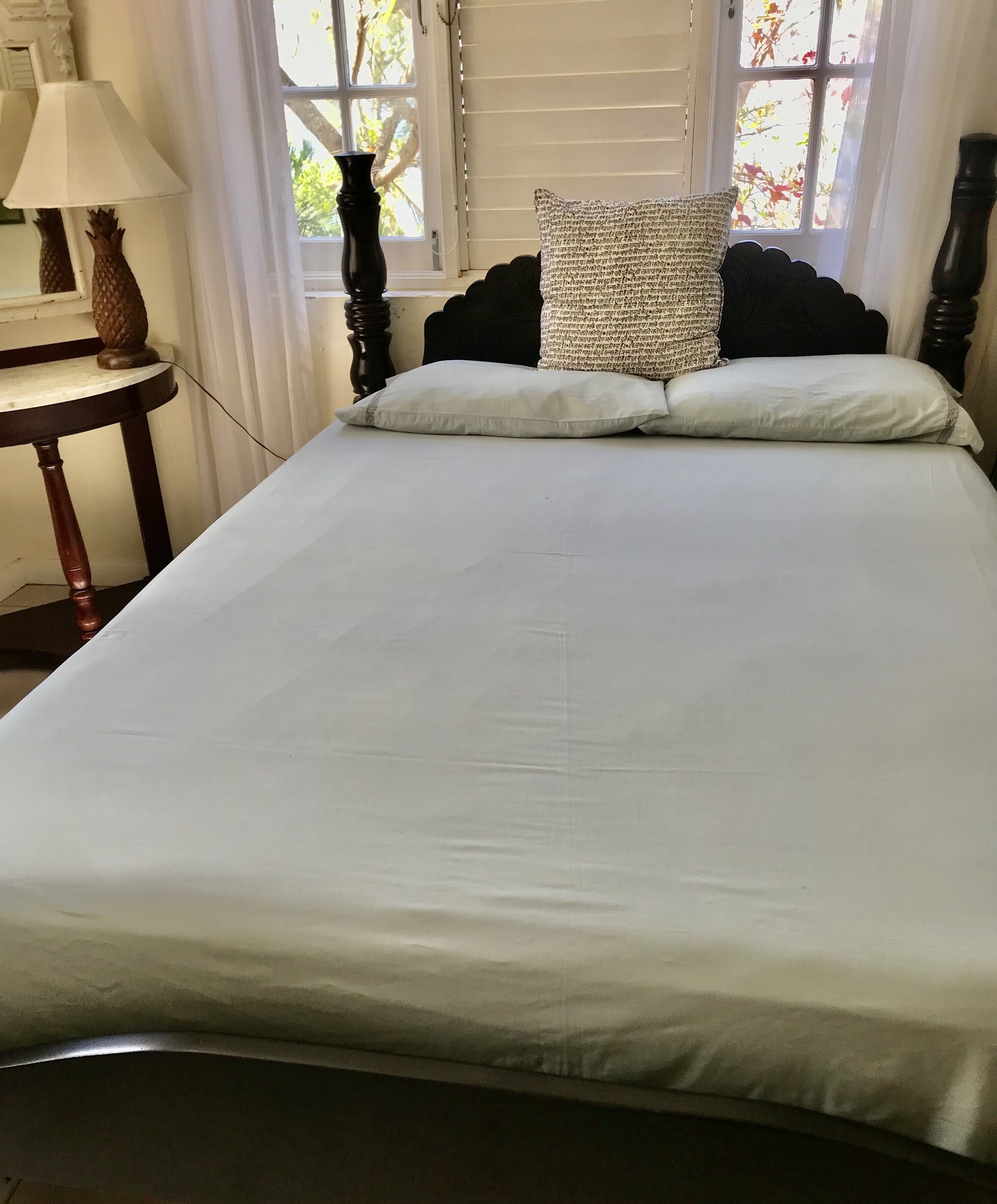 A neatly made bed with white linens, a dark wooden headboard, and a patterned pillow.