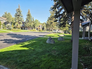 A residential street with houses, a clear sky, and a grassy area with rocks.