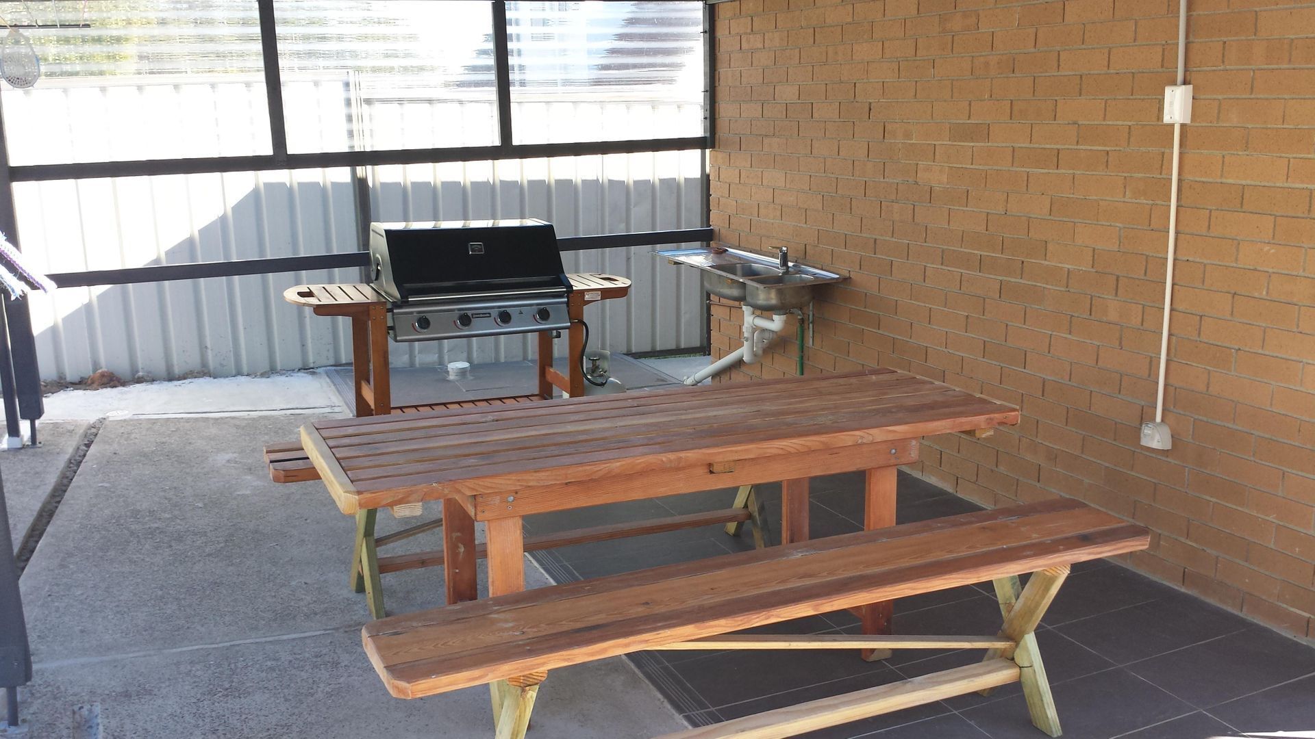 An outdoor patio with a wooden table and bench, a grill, and a sink.