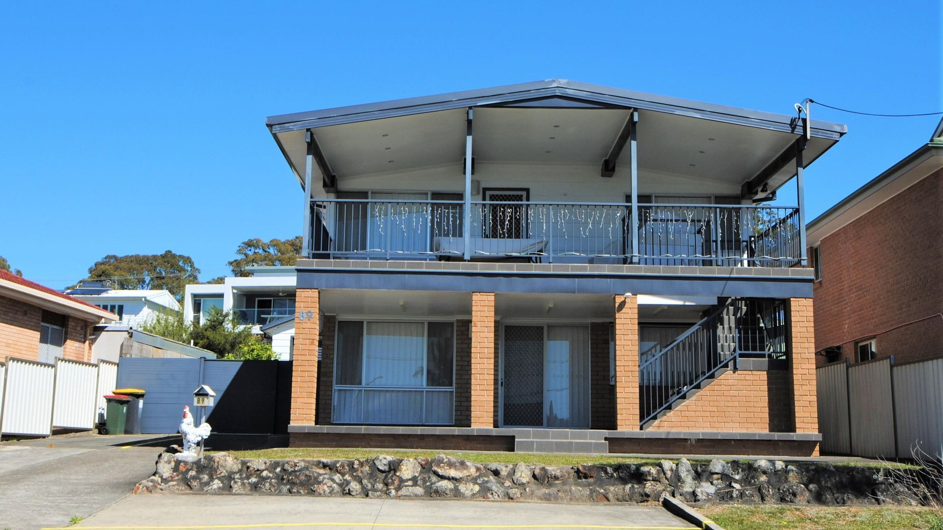 A two-story residential building with a balcony on the upper floor, a stone foundation, and a visible address sign.