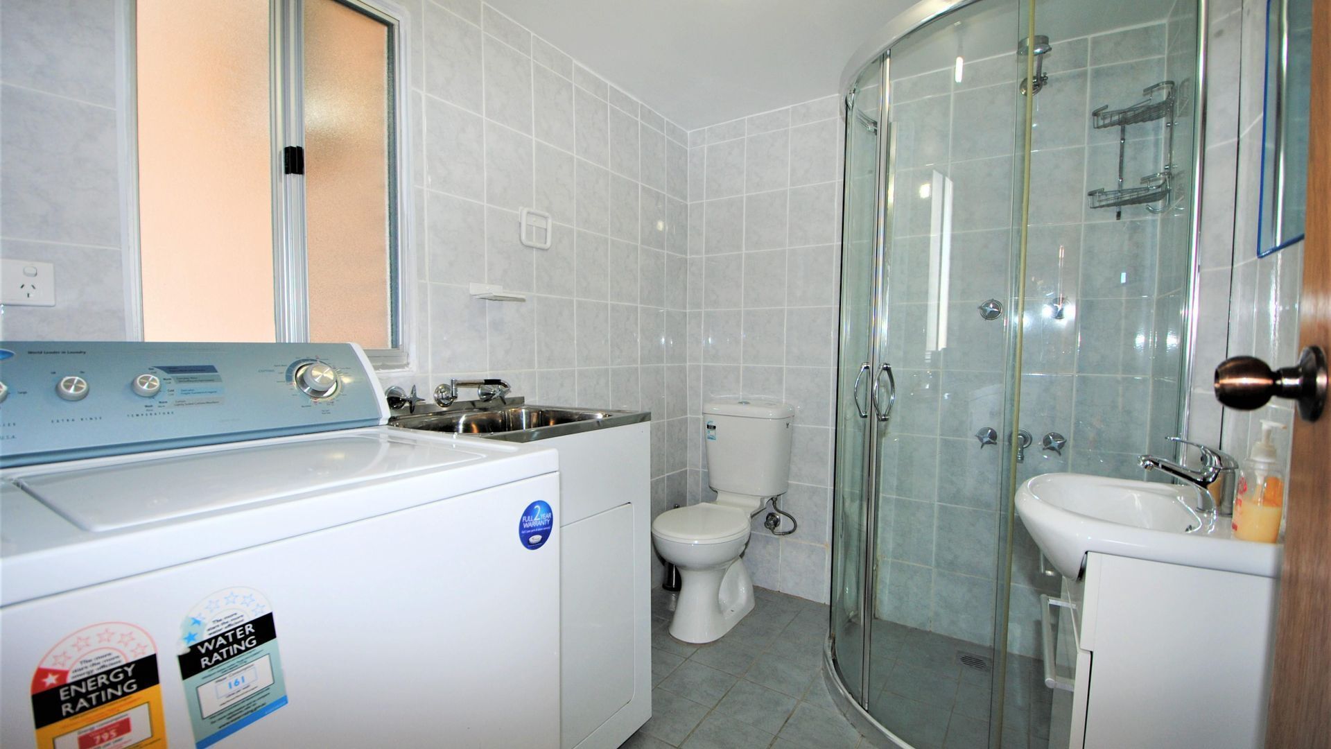 A compact bathroom with a washing machine, toilet, glass shower enclosure, and sink.