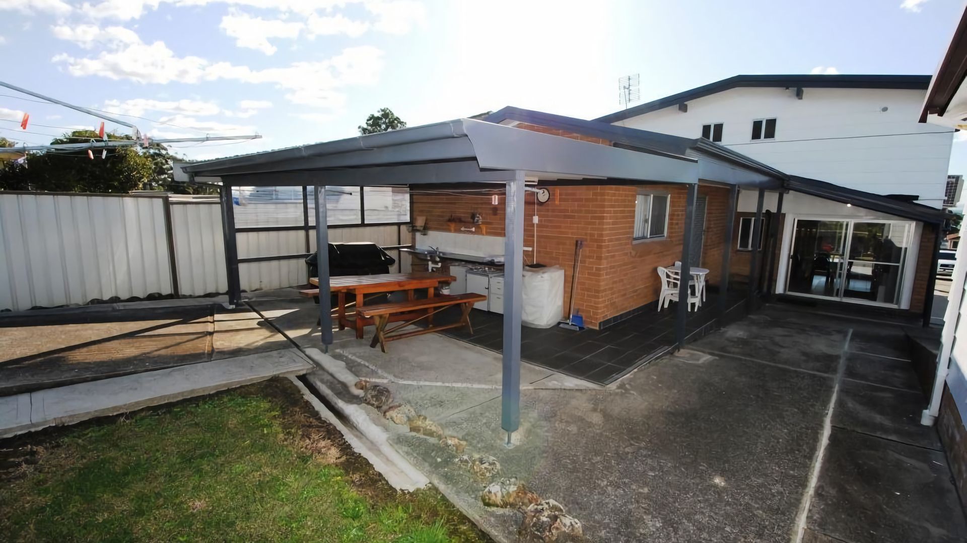A backyard with a covered patio, a barbecue area, and a brick wall.