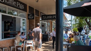 Un espace extérieur aménagé avec des tables et des chaises, appartenant à un restaurant appelé « 5 Little Pigs », avec des murs en briques et de grandes fenêtres.