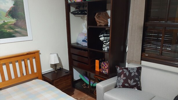 Ein Schlafzimmer mit einem Bett, einem Nachttisch aus Holz, einer Lampe, einem Kleiderschrank und einem grauen Sofa mit einem floralen Kissen.