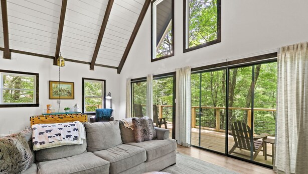 A spacious living room with a large sofa, a coffee table, and a view of a wooden deck through large sliding glass doors. - Renovated, Foosball, In the trees, EV charger! (Beech Mountain)