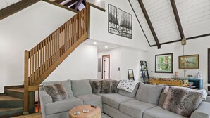 A modern living room with a sectional sofa, a wooden staircase, and a ceiling with exposed beams. - Renovated, Foosball, In the trees, EV charger! (Beech Mountain)