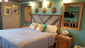 Ein Schlafzimmer mit Bett, Holz-Kopfteil, Nachttischen, einem Spiegel und Wanddekorationen.