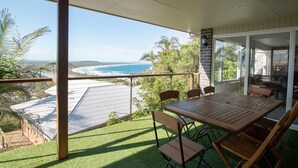 A balcony with a view of the ocean, a wooden table and chairs, and a glass door leading to a patio area.