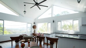 A spacious kitchen with large windows, a dining area with wooden furniture, and a ceiling fan.