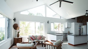 A spacious living area with a high ceiling, large windows, and a kitchen area with modern appliances.