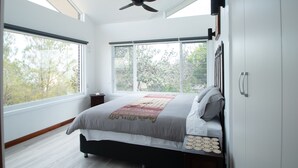 A bedroom with a bed, large windows, a ceiling fan, and a nightstand.