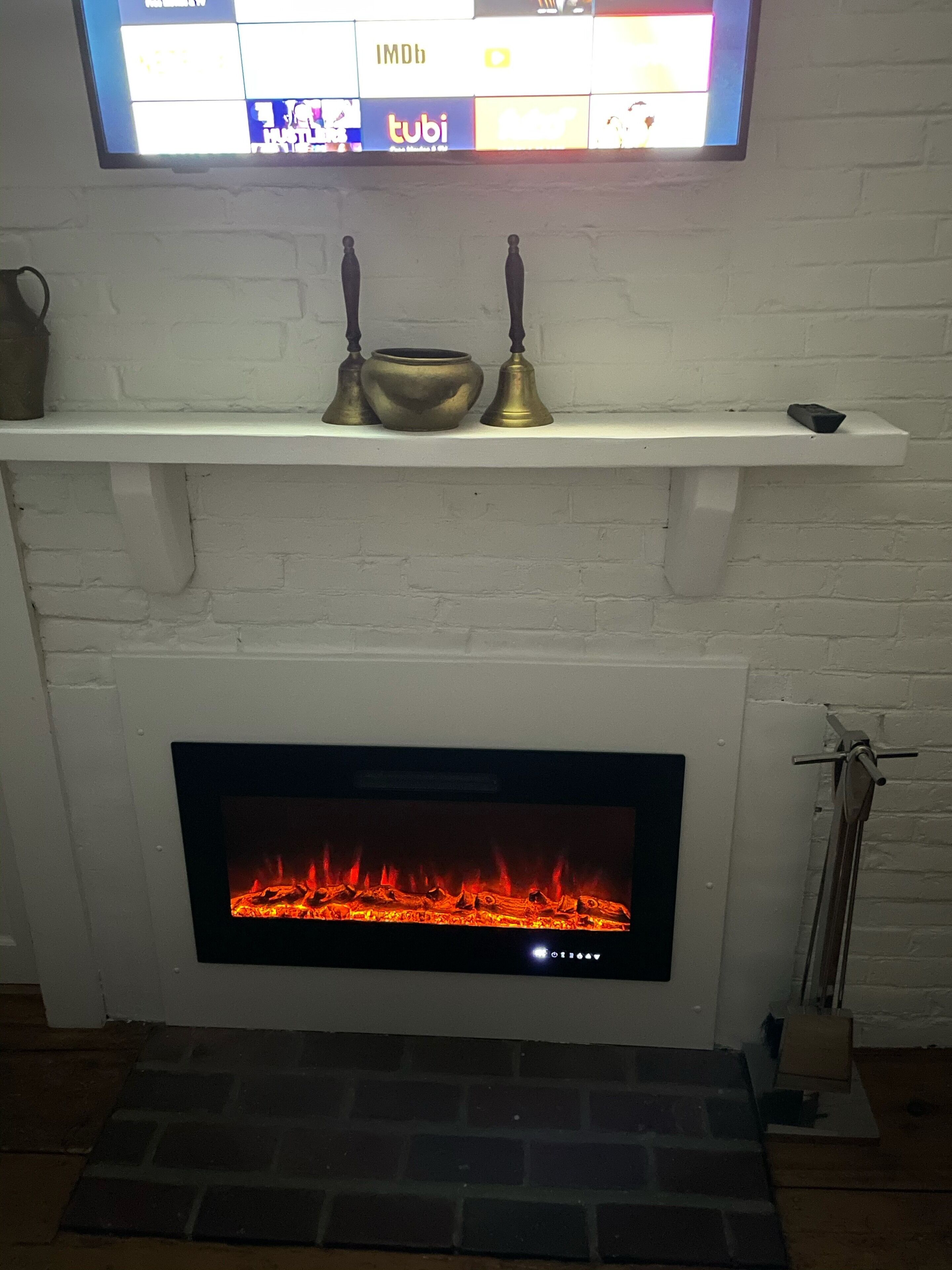 Een haard met een televisie erboven, een plank met decoratieve objecten, en een vlammend vuur.