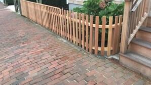 Un camino de ladrillo que lleva a una valla de madera y una casa con porche.