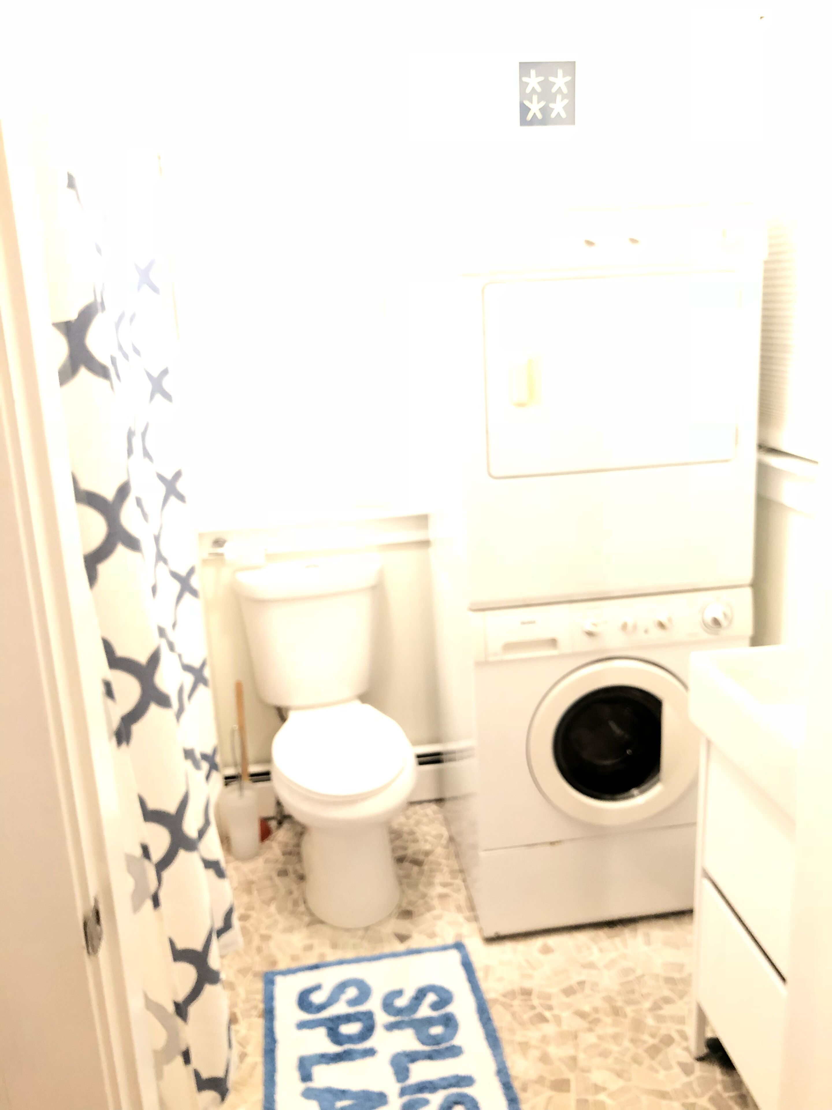 A small, brightly lit bathroom with a toilet, washing machine, and a shower curtain with a star pattern.