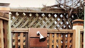 Ducha exterior de madera con puerta metálica y un banco.