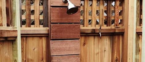 A wooden outdoor shower enclosure with a metal door and a bench.