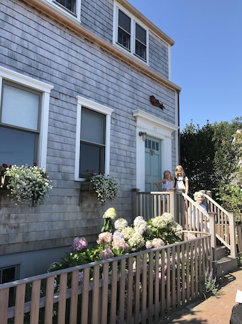 A two-story house with a grey siding exterior, a front porch with a wooden railing, and a small staircase leading to the entrance.