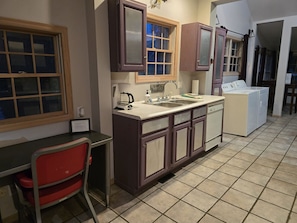 Compact kitchen with sink, coffee maker, dishwasher, and washing machine, featuring a dining area with a small table and chair.