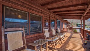 A wooden cabin with a covered porch, large windows, and outdoor seating. - SPECIAL RATES OCT 12-16, MT VIEWS, ATTACHED GARAGE, FLAT PAVED PARKING, PET FEE. (Maggie Valley)