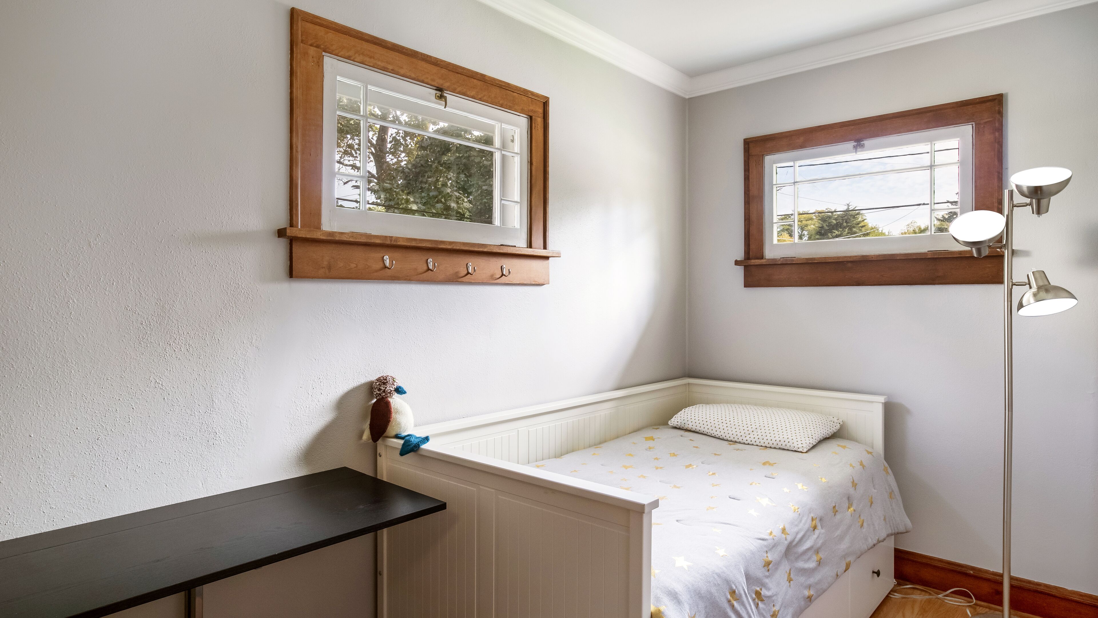 A small, cozy room with a single bed, a nightstand, a window with a wooden frame, and a floor lamp.