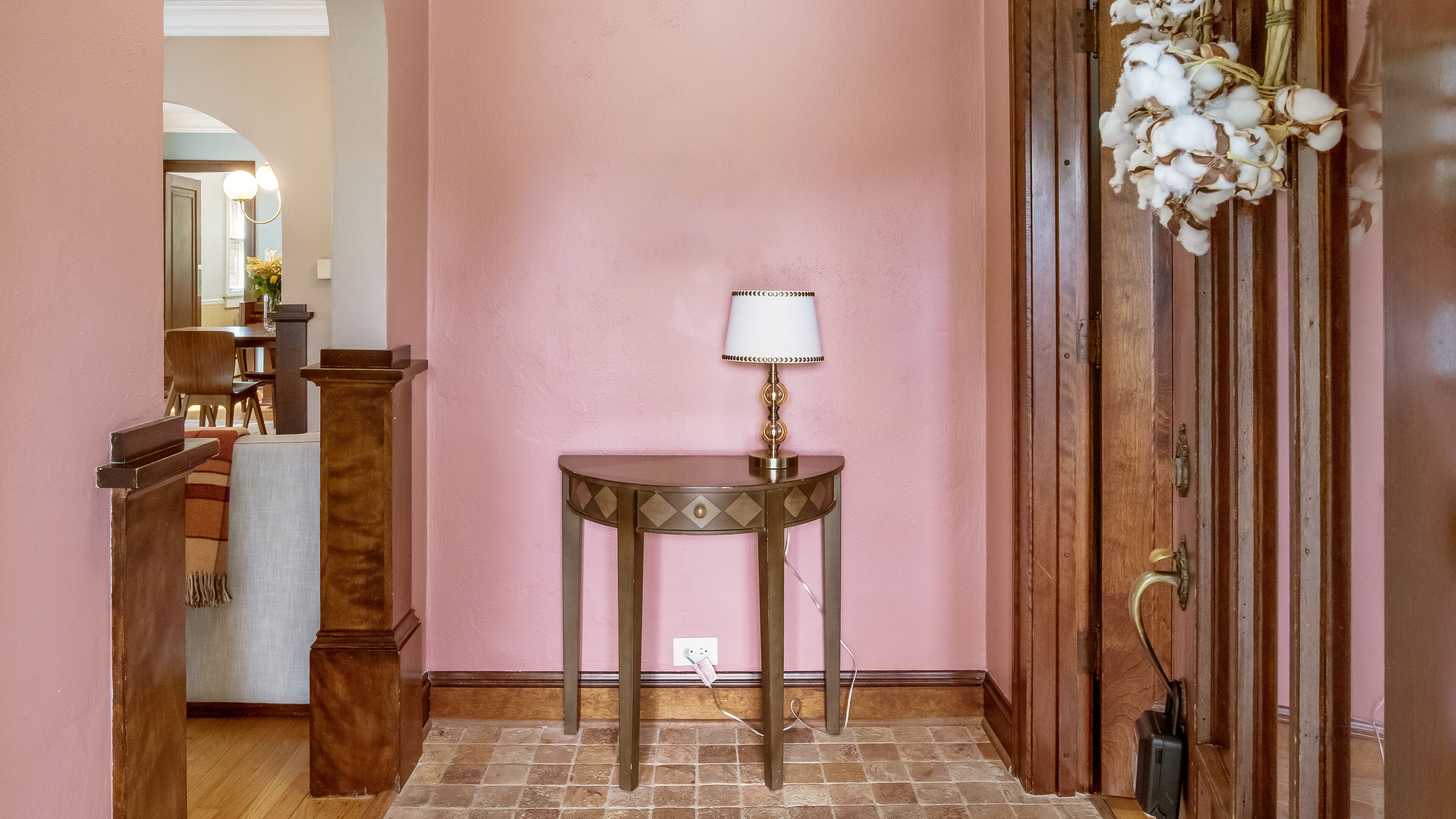 A hallway with pink walls, a wooden door with a glass panel, and a small table with a lamp.