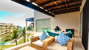 Un balcón con mobiliario de madera, vista a una piscina y un paisaje urbano al fondo.