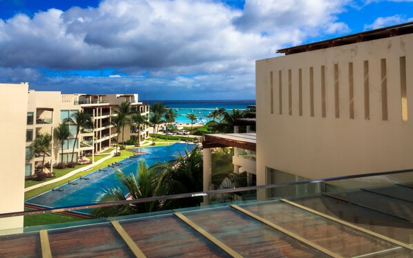 A resort with a large swimming pool, a view of the ocean, and a tropical setting with palm trees.