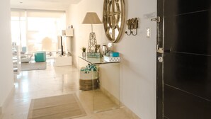 Un pasillo amplio con una puerta negra, una mesa de centro de vidrio, una lámpara y un espejo decorativo.