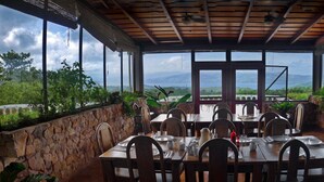 An outdoor dining area with stone walls, wooden tables, and chairs, overlooking a mountainous landscape. - Simply the best, incredible views, pool, breakfast and a friend in the area! (Nuevo Arenal/Tilaran)