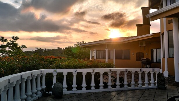 A house with a balcony, a view of the sunset, and a garden with various plants. - Simply the best, incredible views, pool, breakfast and a friend in the area! (Nuevo Arenal/Tilaran)