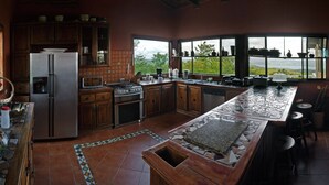 A spacious kitchen with a large island, wooden cabinets, and a view of the outdoors through large windows. - Simply the best, incredible views, pool, breakfast and a friend in the area! (Nuevo Arenal/Tilaran)