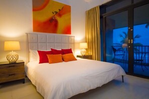 Une chambre d’hôtel avec un grand lit, deux tables de chevet avec des lampes, une grande fenêtre donnant sur des palmiers et un tableau au mur.