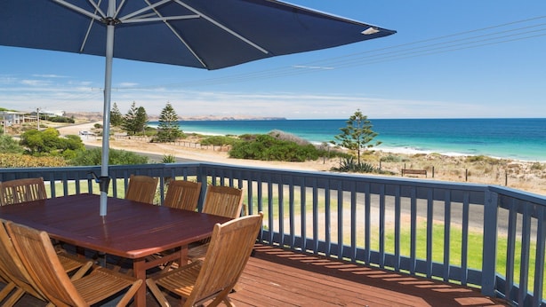 A wooden deck with a table and chairs, overlooking a beach with clear blue waters and a distant shoreline. - Sandy Feet - 31 Gold Coast Drive (CARRICKALINGA)