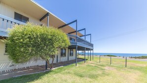 A two-story building with a balcony overlooking a grassy area and a view of the ocean. - Sandy Feet - 31 Gold Coast Drive (CARRICKALINGA)