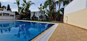A swimming pool with lounge chairs and a covered seating area, surrounded by palm trees and a white building. - Villa With Private Pool, Sea View With Grass And 2 Gazebos (Pernera)
