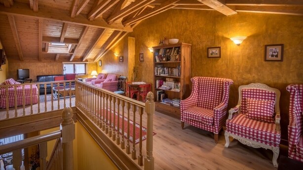 A cozy living room with a wooden ceiling, checkered chairs, a bookshelf, and a television.