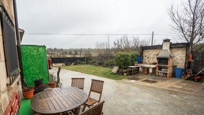 A patio with a round wooden table and chairs, a stone barbecue grill, and a green screen.