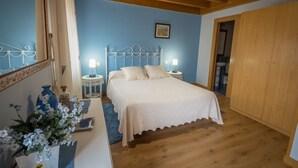 A bedroom with a bed, bedside lamps, a mirror, a wooden wardrobe, and a blue wall.