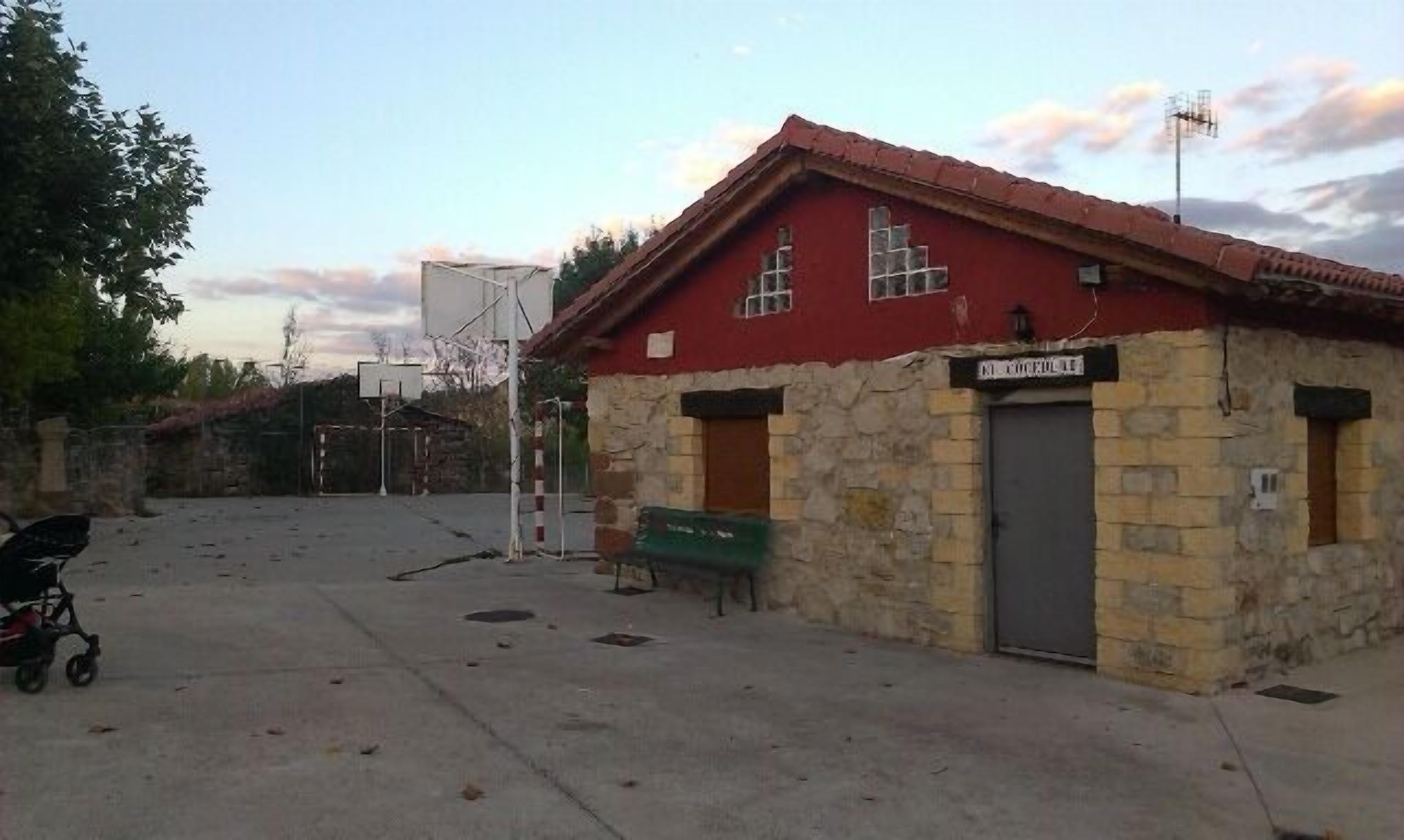 Ein kleines Steinhaus mit rotem Dach, einem Basketballkorb und einer Bank.