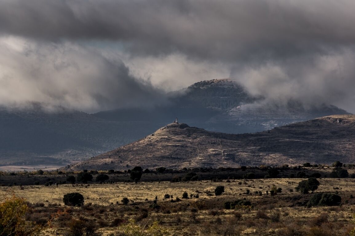 A mountainous landscape with a prominent hill and a small structure on top.