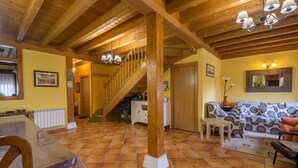 A spacious living area with a wooden staircase, a dining table, and a patterned sofa.