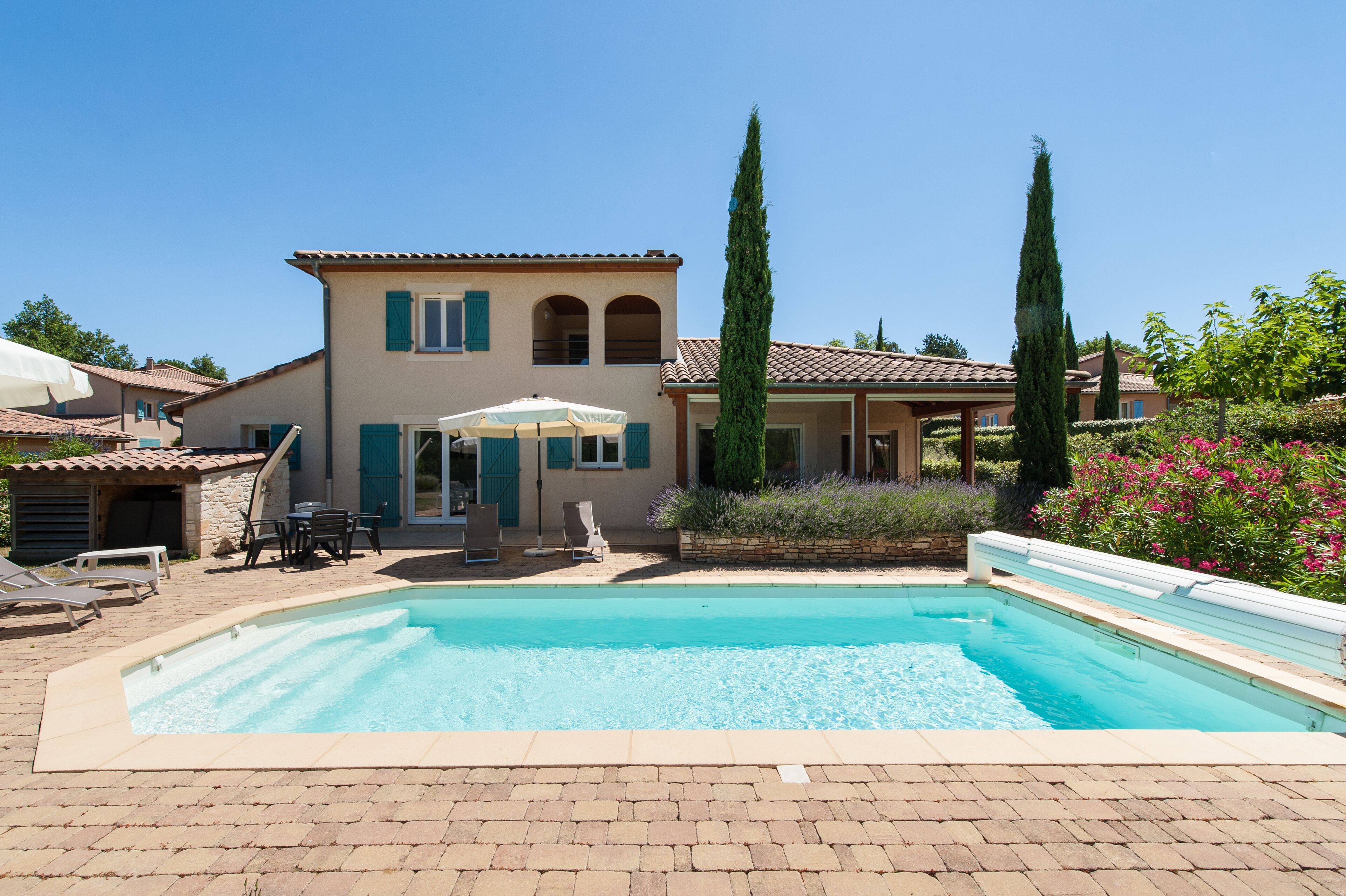A poolside area with a swimming pool, outdoor seating, and a building with a tiled roof.