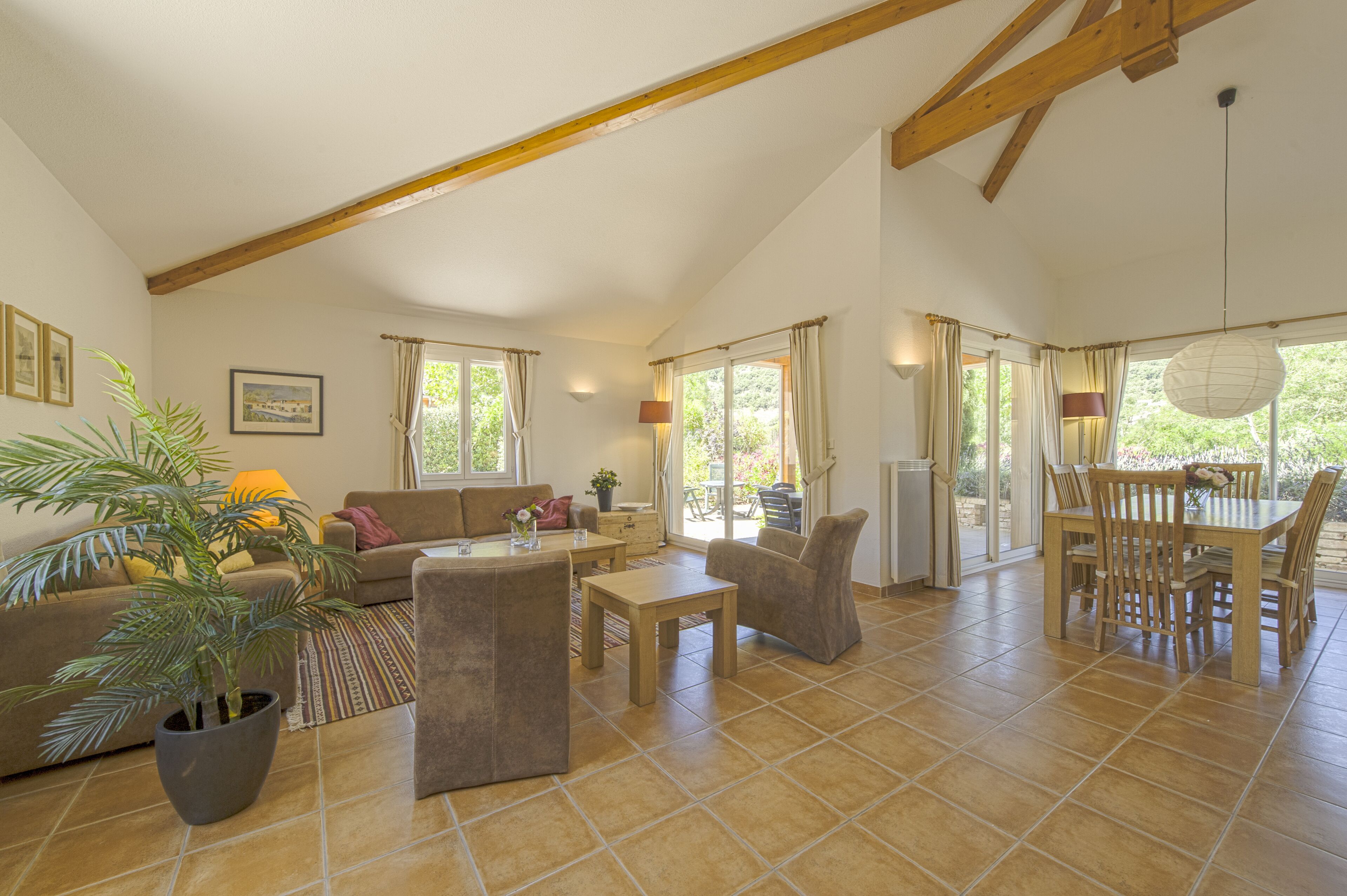 A spacious living area with a high ceiling, a dining table with chairs, a sofa, a coffee table, and a potted plant.