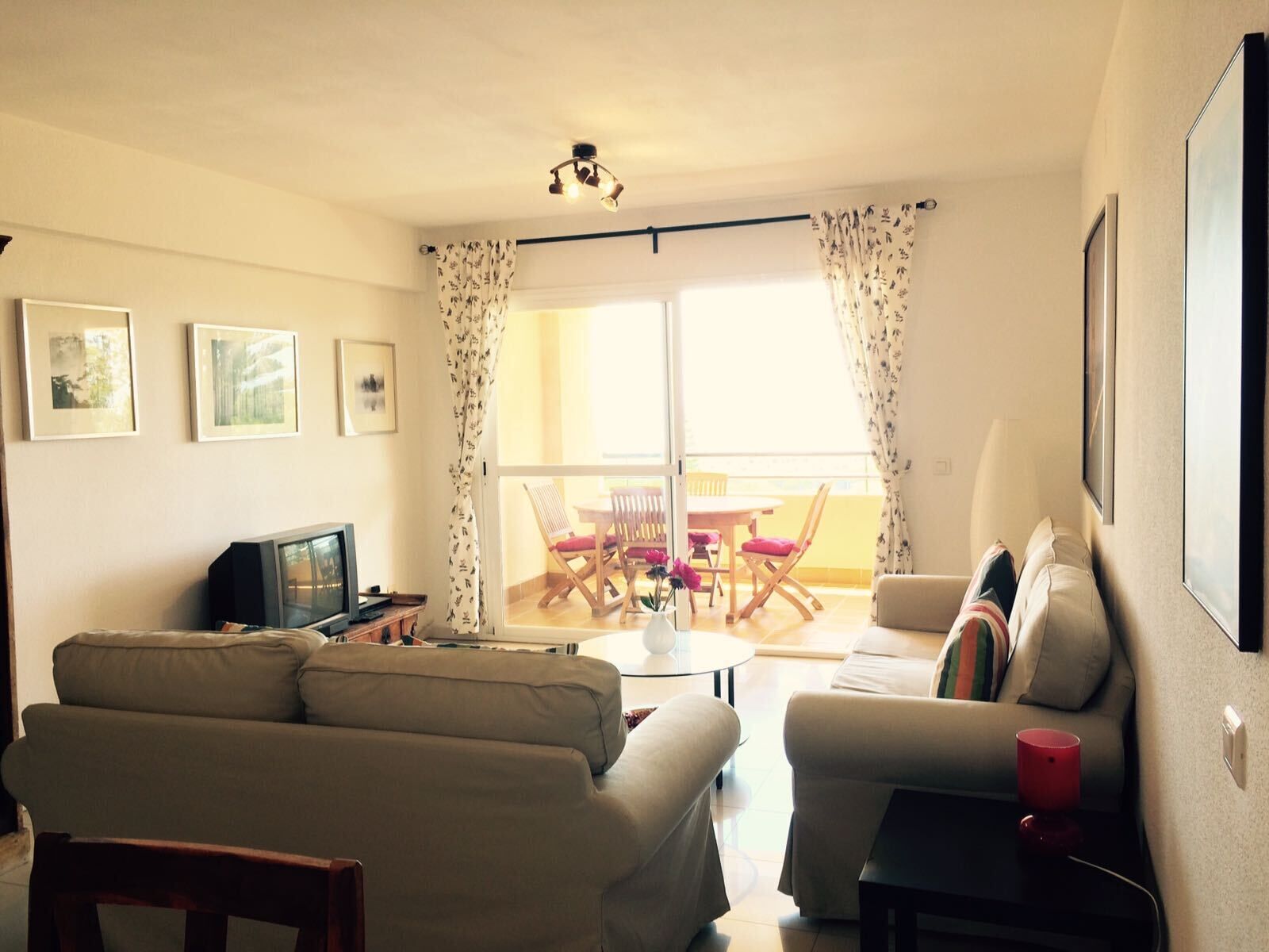 Un salon avec un canapé, un téléviseur, une table avec des chaises et un balcon offrant une vue dégagée.