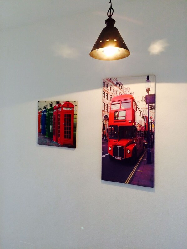 Un mur orné de deux tableaux encadrés : l’un représente des autobus à deux étages rouges, l’autre, des cabines téléphoniques rouges et vertes.
