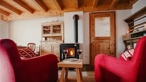 A cozy living room with a wood-burning stove, two red armchairs, a wooden cabinet, and a dining area with a table and chairs.