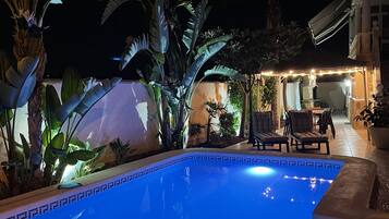 Una piscina con borde de azulejos, rodeada de plantas en macetas y mobiliario de exterior.