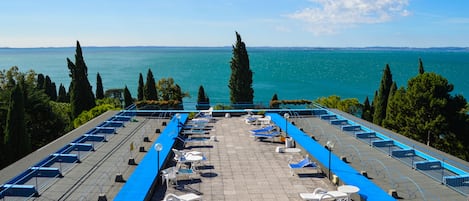 A terrace with sun loungers and tables overlooking a body of water.