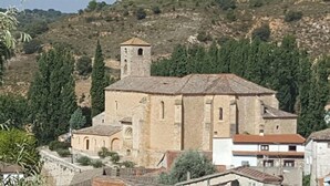 Une église historique en pierre, dotée d’un clocher, entourée de verdure et de bâtiments résidentiels.