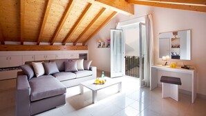 Een moderne woonkamer met een grijze hoekbank, een witte salontafel met fruit, een witte console met een spiegel, en een balkon met een glazen deur.
